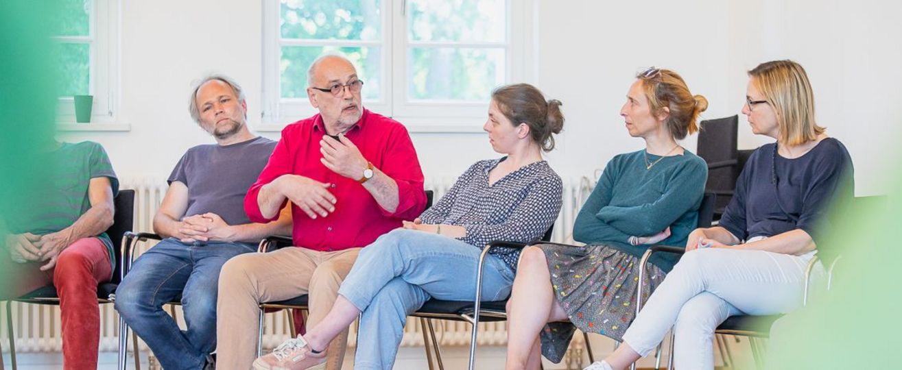 5 Menschen sitzen nebeneinander, einer spricht.