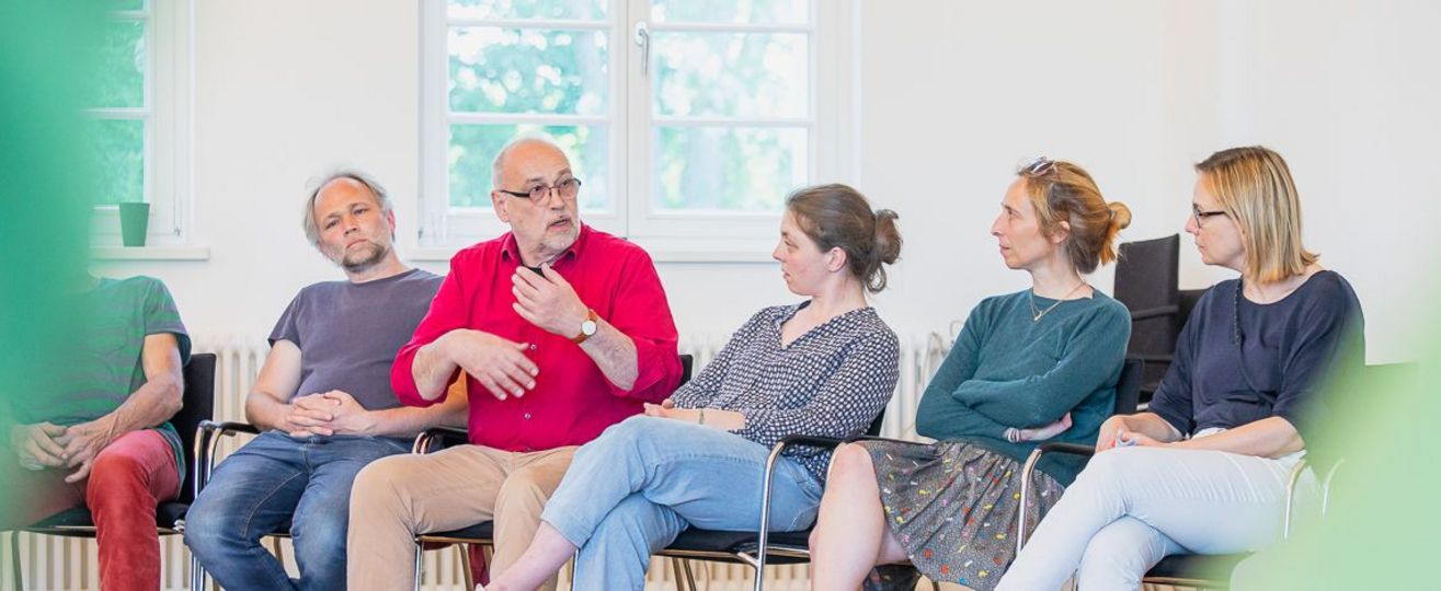 5 Menschen sitzen nebeneinander, einer spricht.