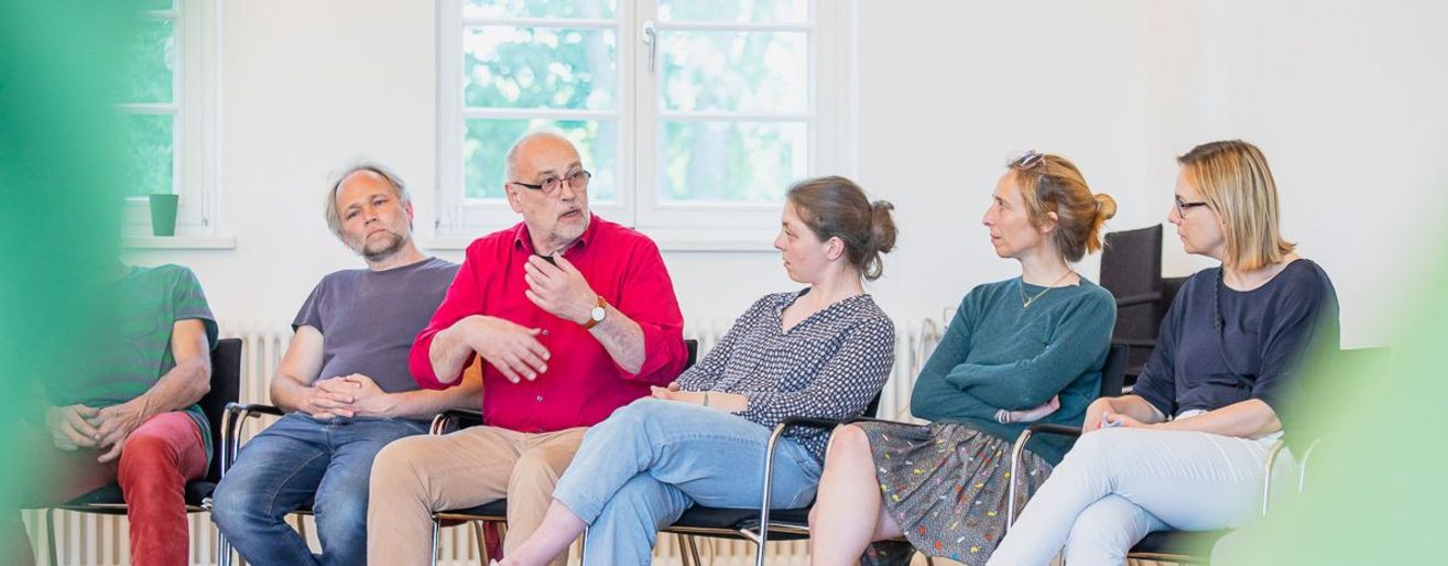 5 Menschen sitzen nebeneinander, einer spricht.