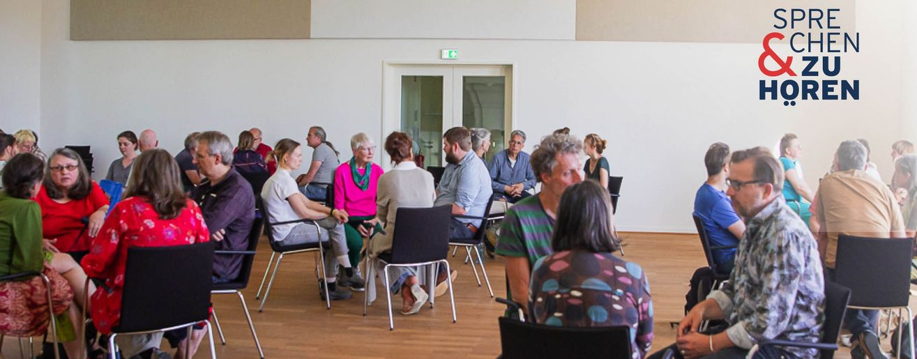 Foto einer Sprechen-und-Zuhören-Veranstaltung mit Menschen auf Stühlen in Gruppen sitzend