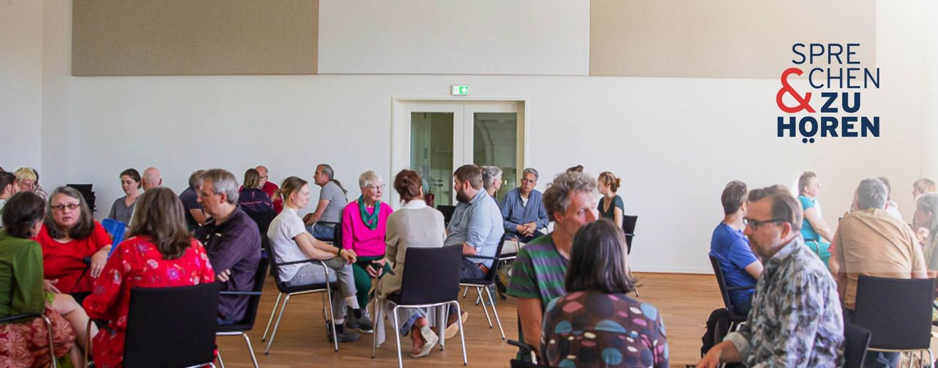 Foto einer Sprechen-und-Zuhören-Veranstaltung mit Menschen auf Stühlen in Gruppen sitzend