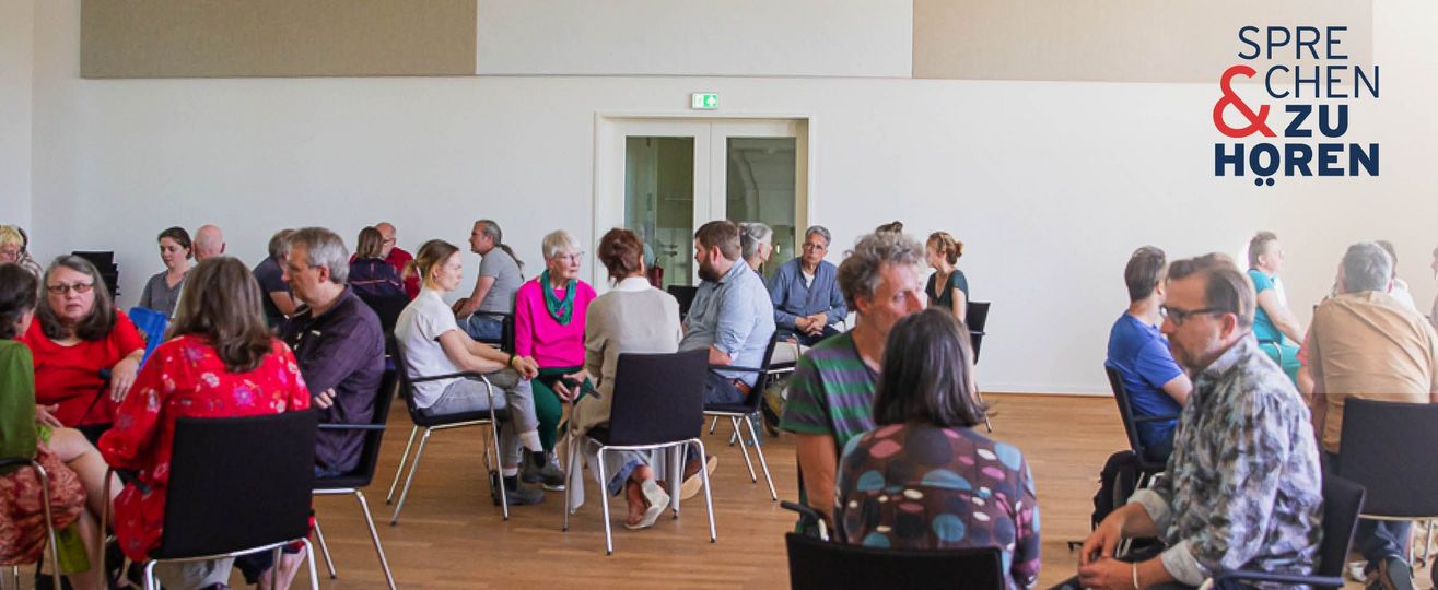 Foto einer Sprechen-und-Zuhören-Veranstaltung mit Menschen auf Stühlen in Gruppen sitzend