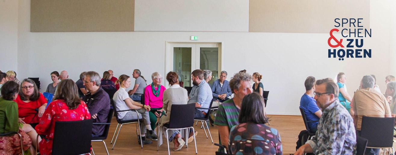 Menschen in Stuhlkreisen (3-4 Personen) in einem hellen Saal, oben rechts das Logo „Sprechen & Zuhören".