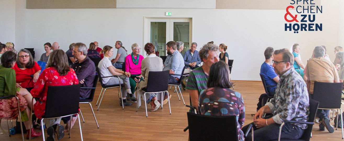 Foto einer Sprechen-und-Zuhören-Veranstaltung mit Menschen auf Stühlen in Gruppen sitzend