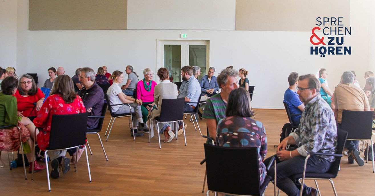 Foto einer Sprechen-und-Zuhören-Veranstaltung mit Menschen auf Stühlen in Gruppen sitzend